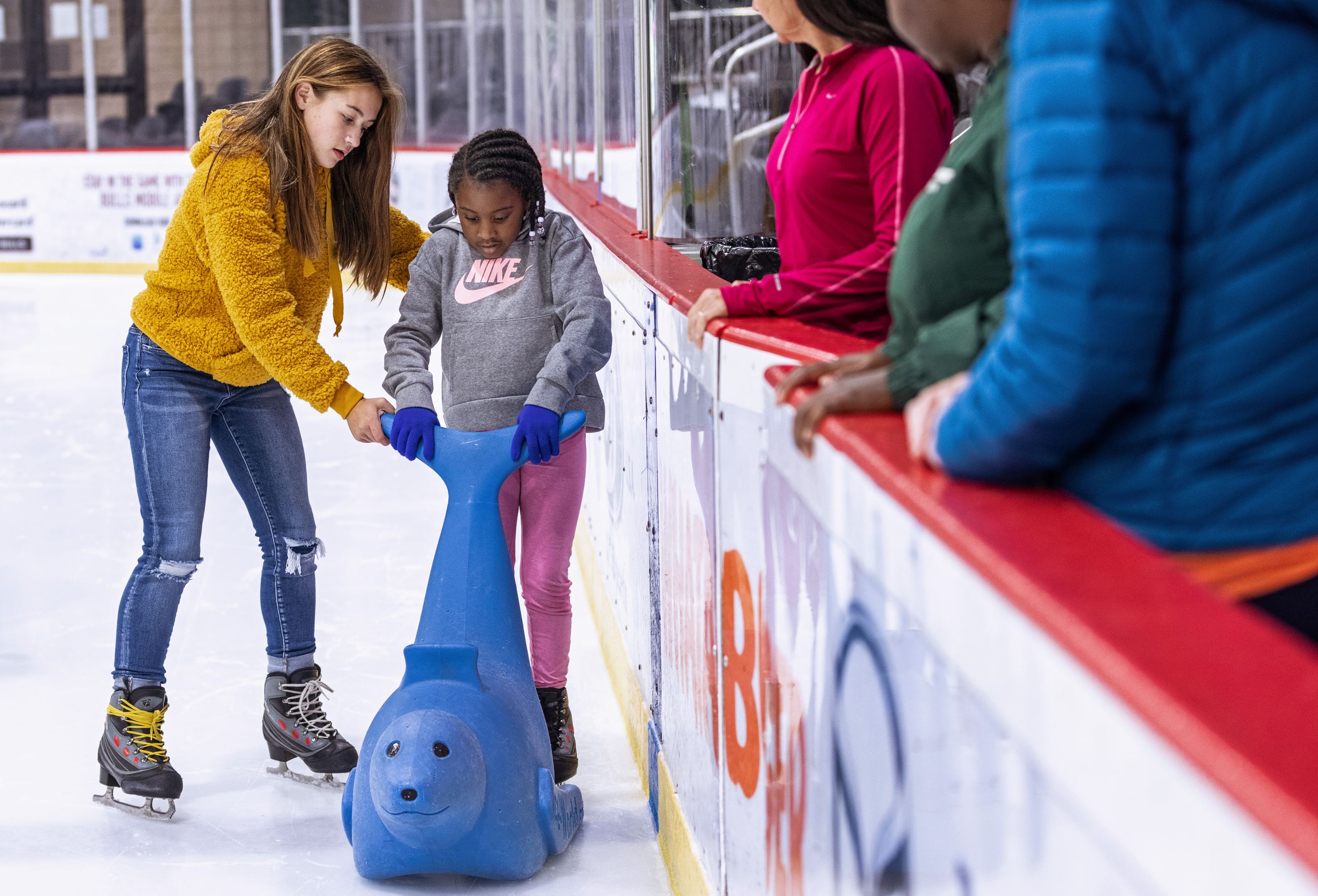 Teenage girl helping young girl ice skate