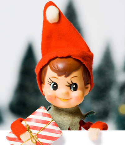 Image shows an elf holding a Christmas gift against a background of Christmas trees.