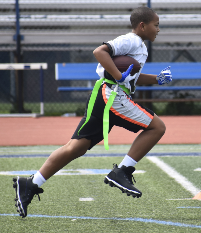 Young boy running with football wearing flag football equipment on his waist